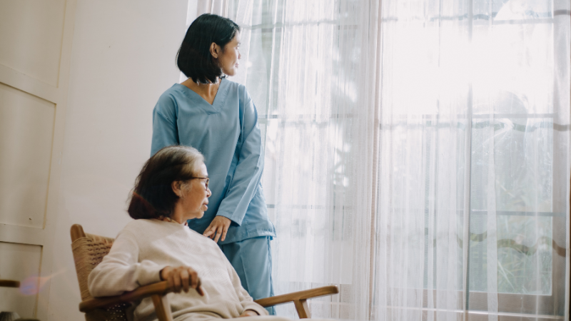 When to Call Hospice for Dementia - younger woman standing next to older woman in rocking chair. 